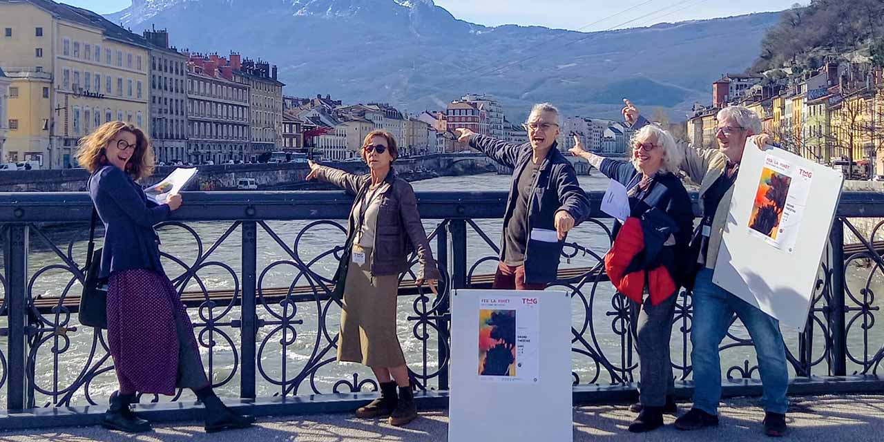 5 complices sont sur le pont piéton au dessus de l'Isère et tiennent des affiches du spectacle Feu la forêt