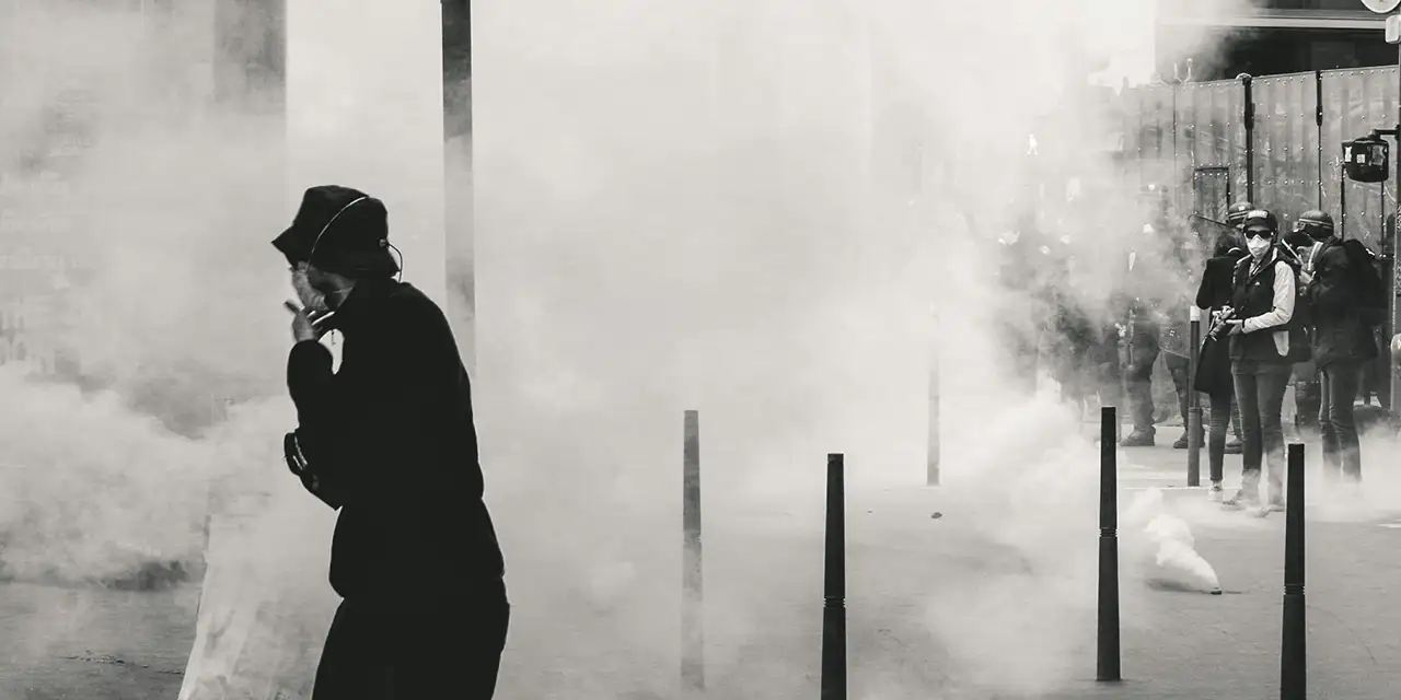 Un homme masqué dans une manifestation entouré de fumée