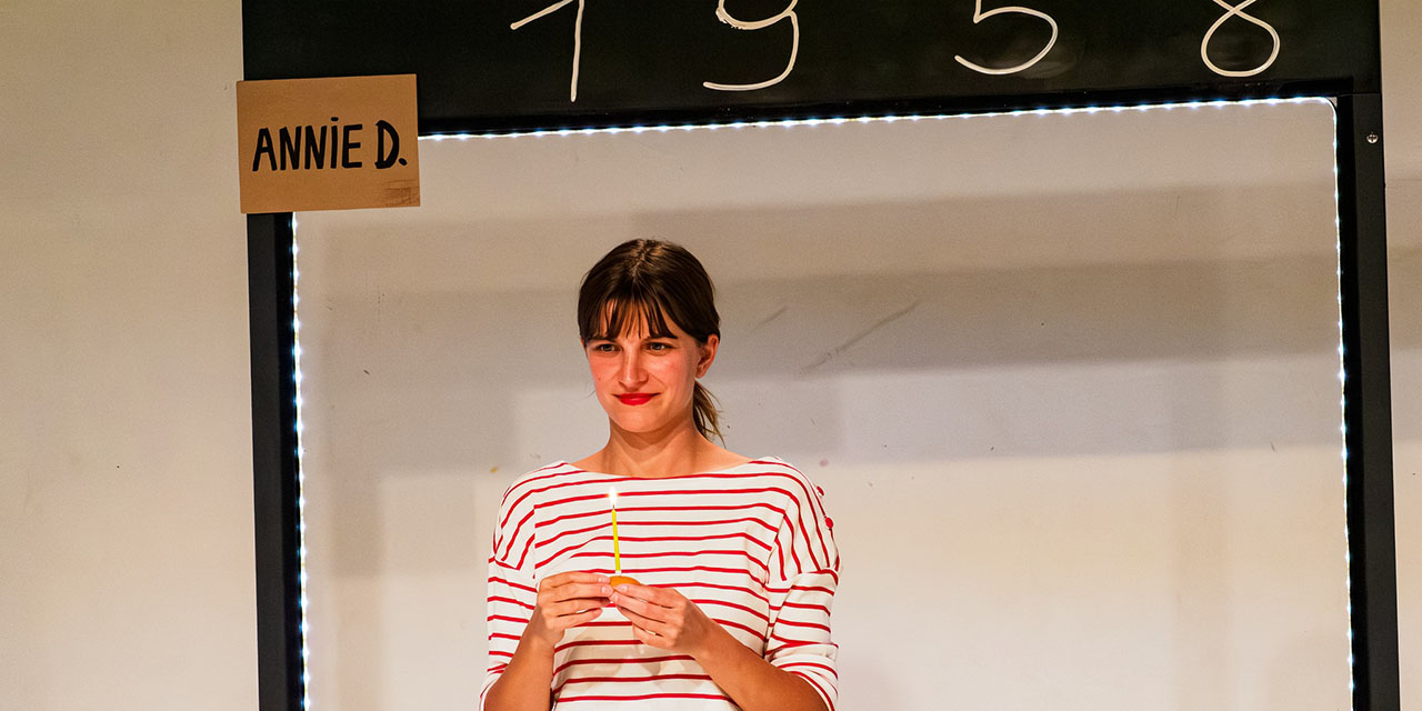 La comédienne se tient face à nous avec une bougie jaune entre les mains
