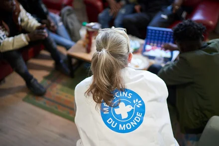 Une bénévole des Médecins du monde de dos, accroupie auprès d'un groupe de personne.