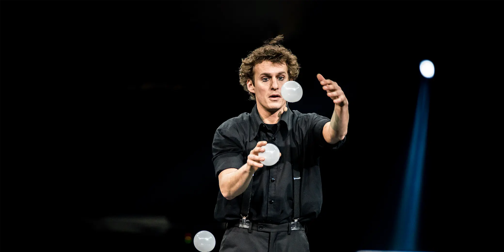 Un artiste vêtu d'une chemise noire jongle avec des balles blanches