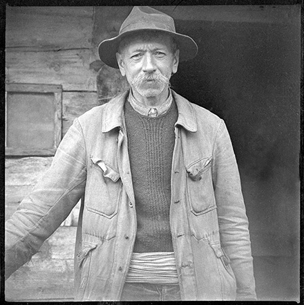 Portrait d'un vieil homme en noir et blanc devant une maison