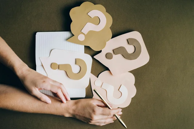 Deux mains posées autour d'éléments en papier marqués de points d'interrogation.