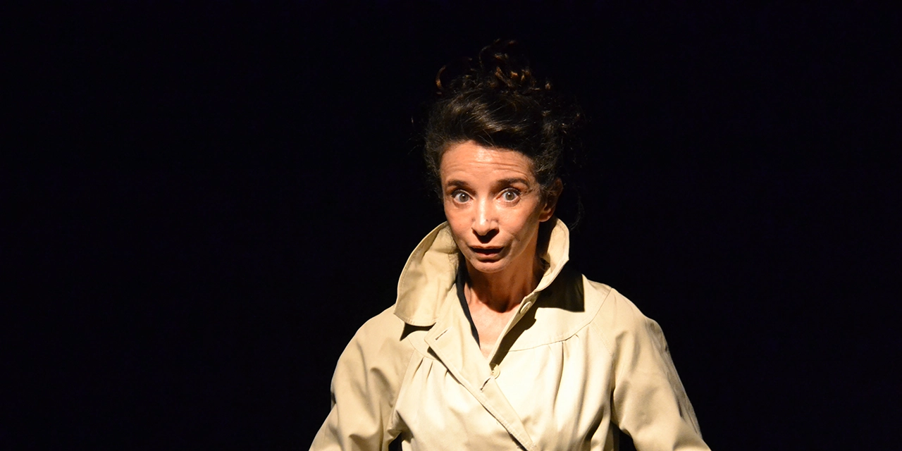 La comédienne se tient debout, elle porte un trench beige.