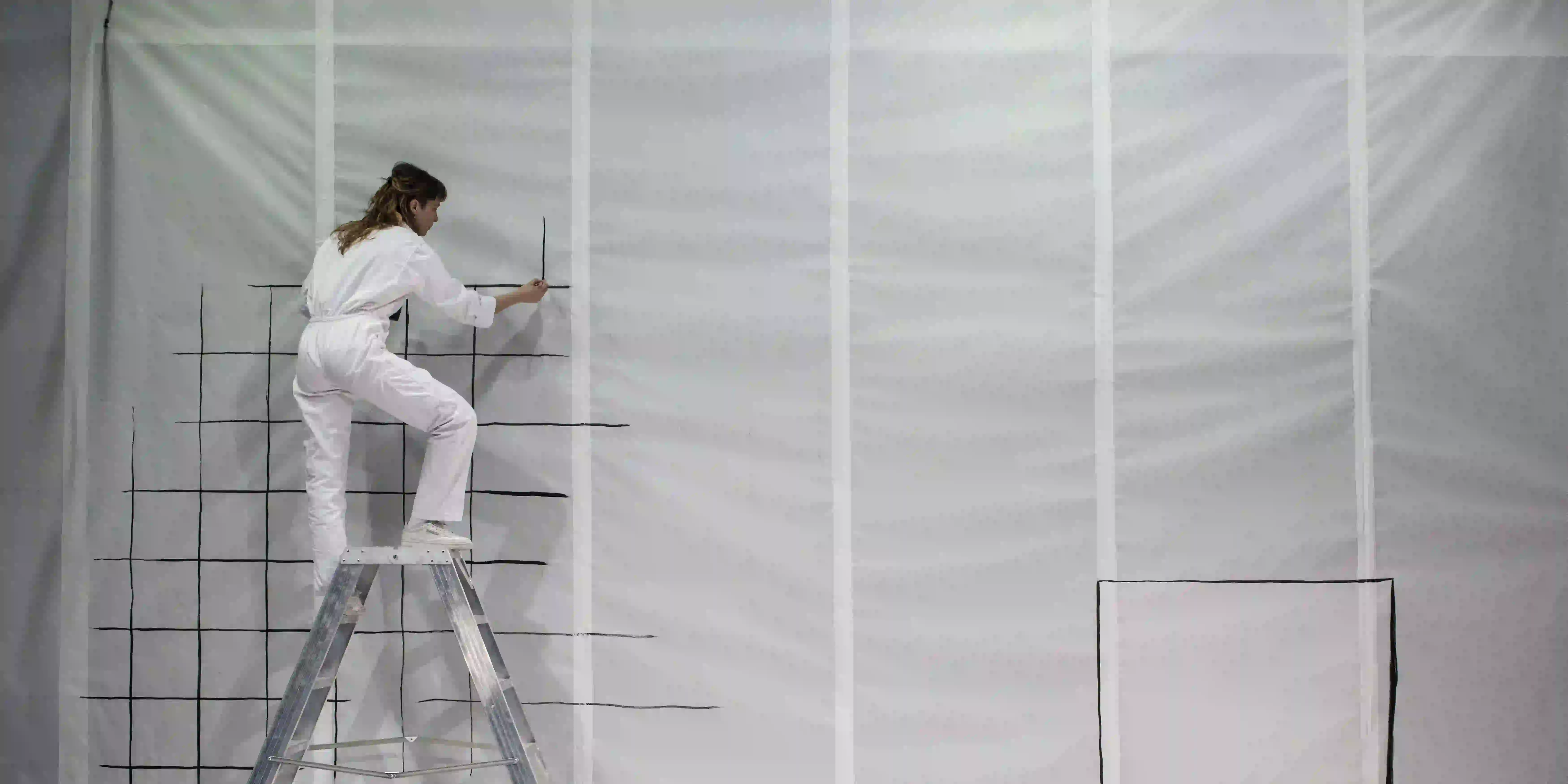La comédienne est perchée sur un escabot, elle paint une toile blanche