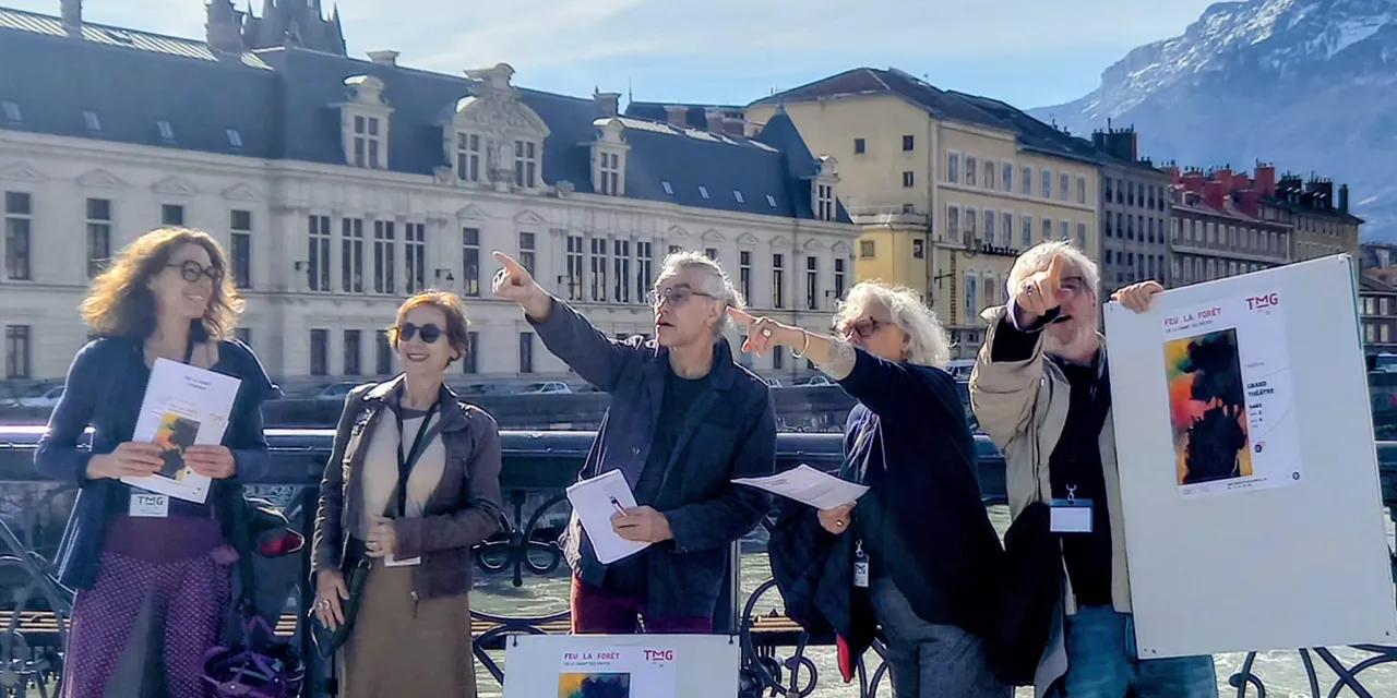 5 membres des Complices sont souriant côte à côte sur un pont, certains pointent l'horizon.