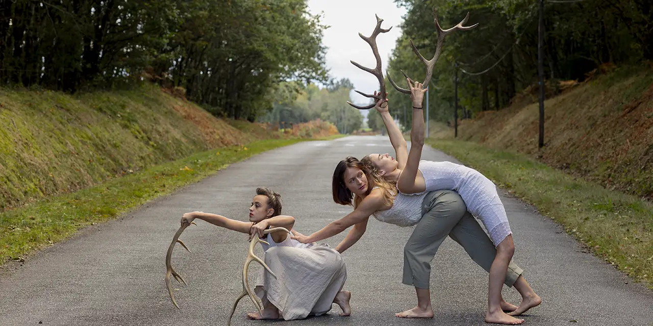 Les trois danseuses sont sur une route, elles tiennent des bois de cerf
