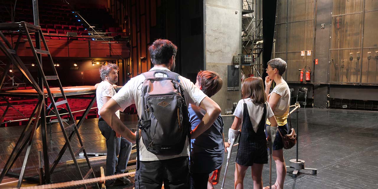 4 personnes sont sur le plateau du Grand Théâtre de dos, ils font face à un technicien du TMG devant une structure de décor de spectacle