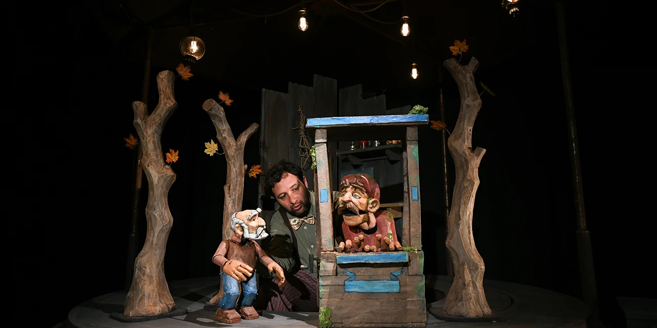Le comédien tient deux marionnettes dans un décor de forêt