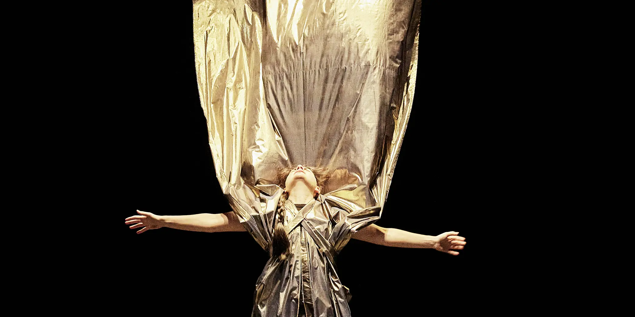 Une comédienne, les bras en croix, lève la tête vers le ciel et le pan arrière de sa robe s'envole.