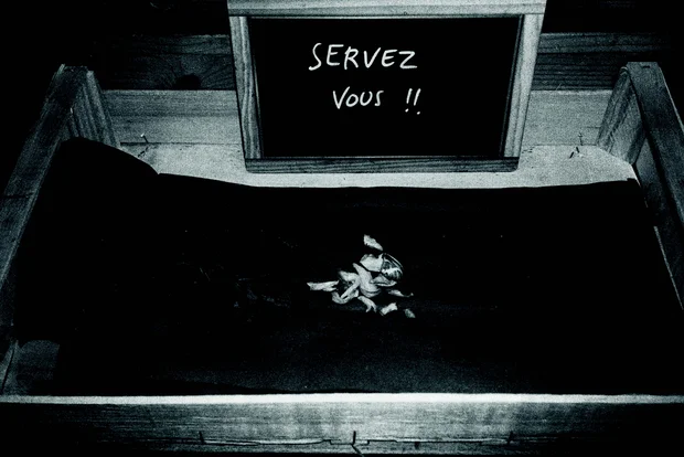 Une cagette en bois comprend des restes insignifiants de nourriture. Une ardoise apposée au dessus indique "Servez-vous !"