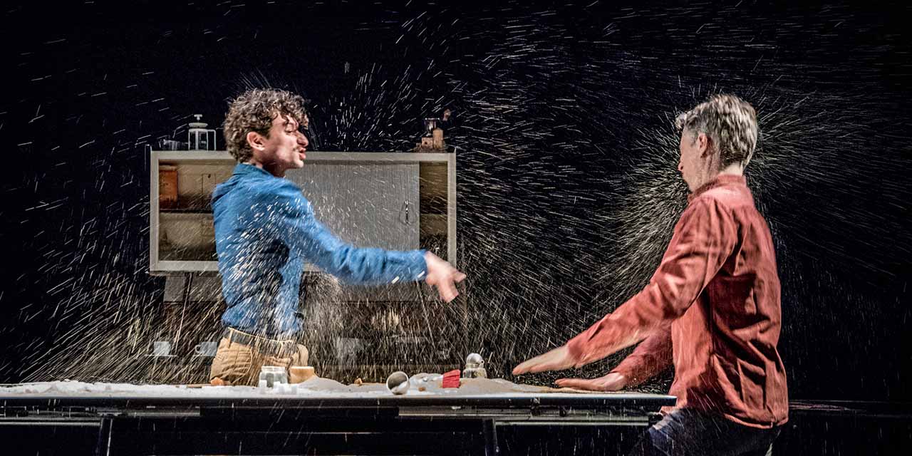 Deux comédiens se lancent de l'eau dans un décor de cuisine.