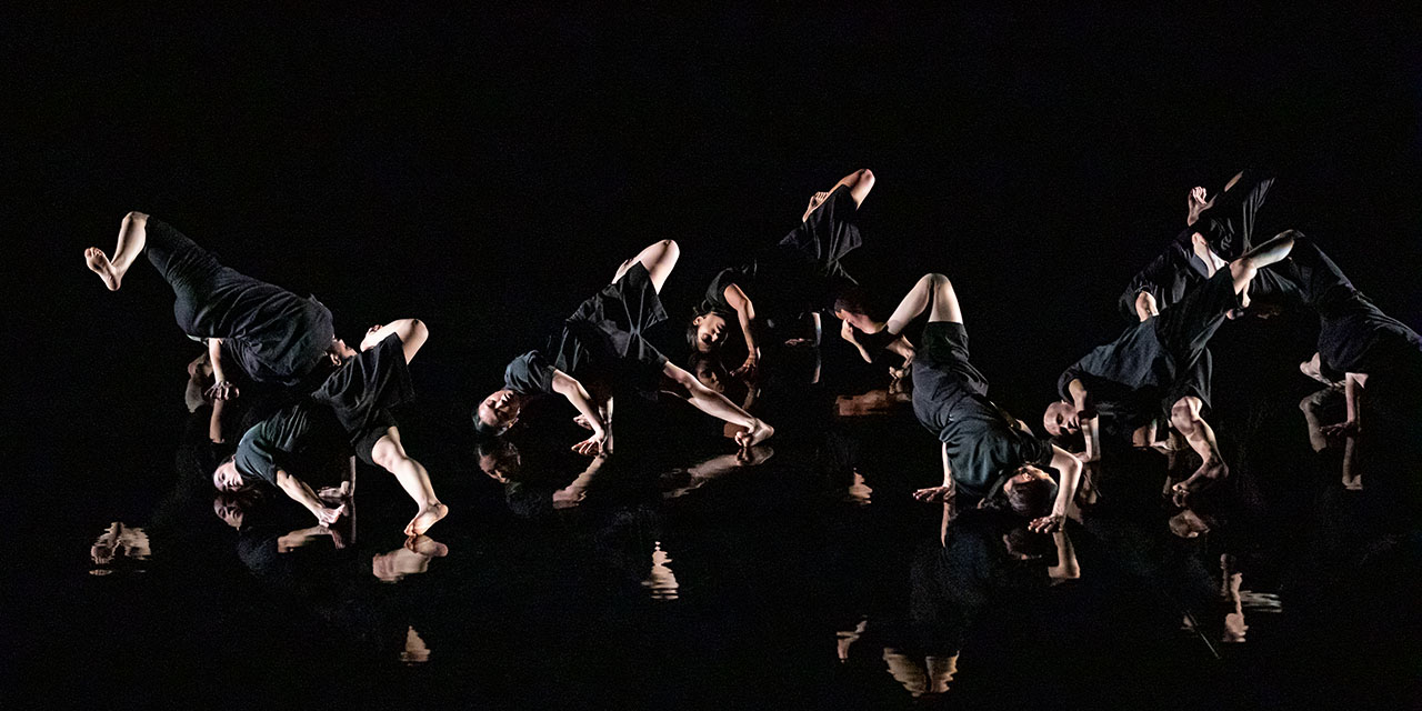 8 danseurs et danseuses font une figure sur un sol noir, tout le monde portent du noir.