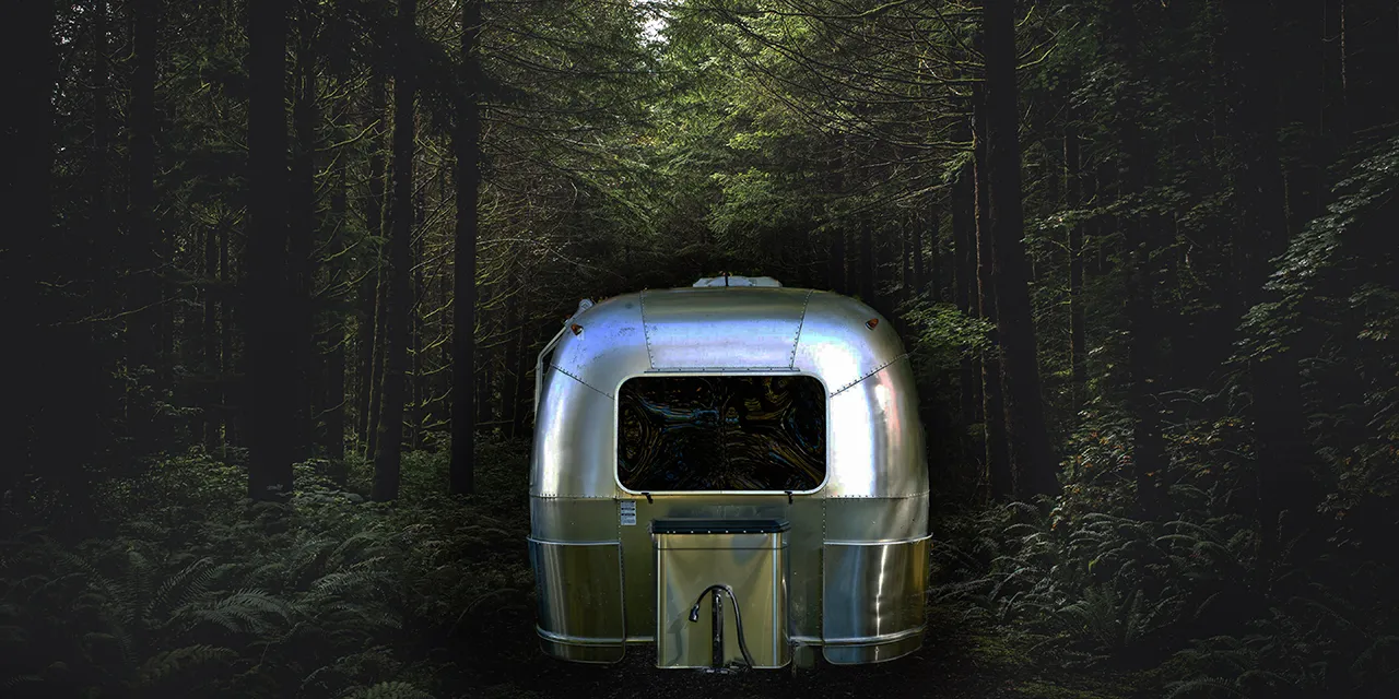 Un mobile home gris est garé dans une forêt