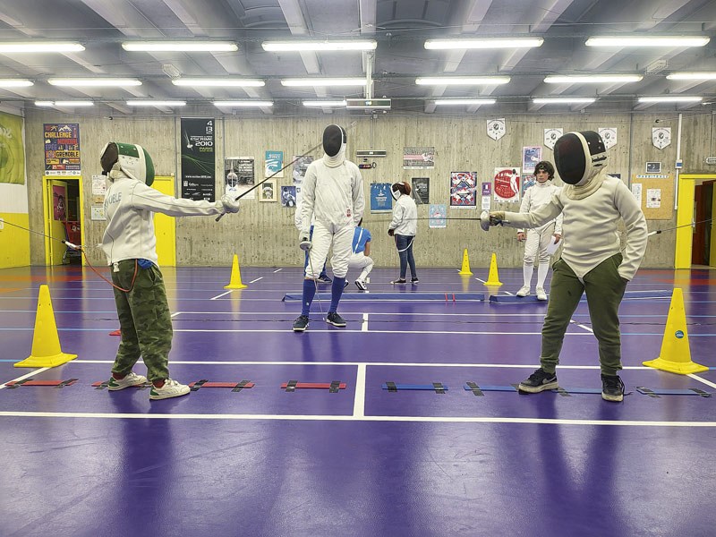 Des enfants font de l'escrime dans un gymnase.