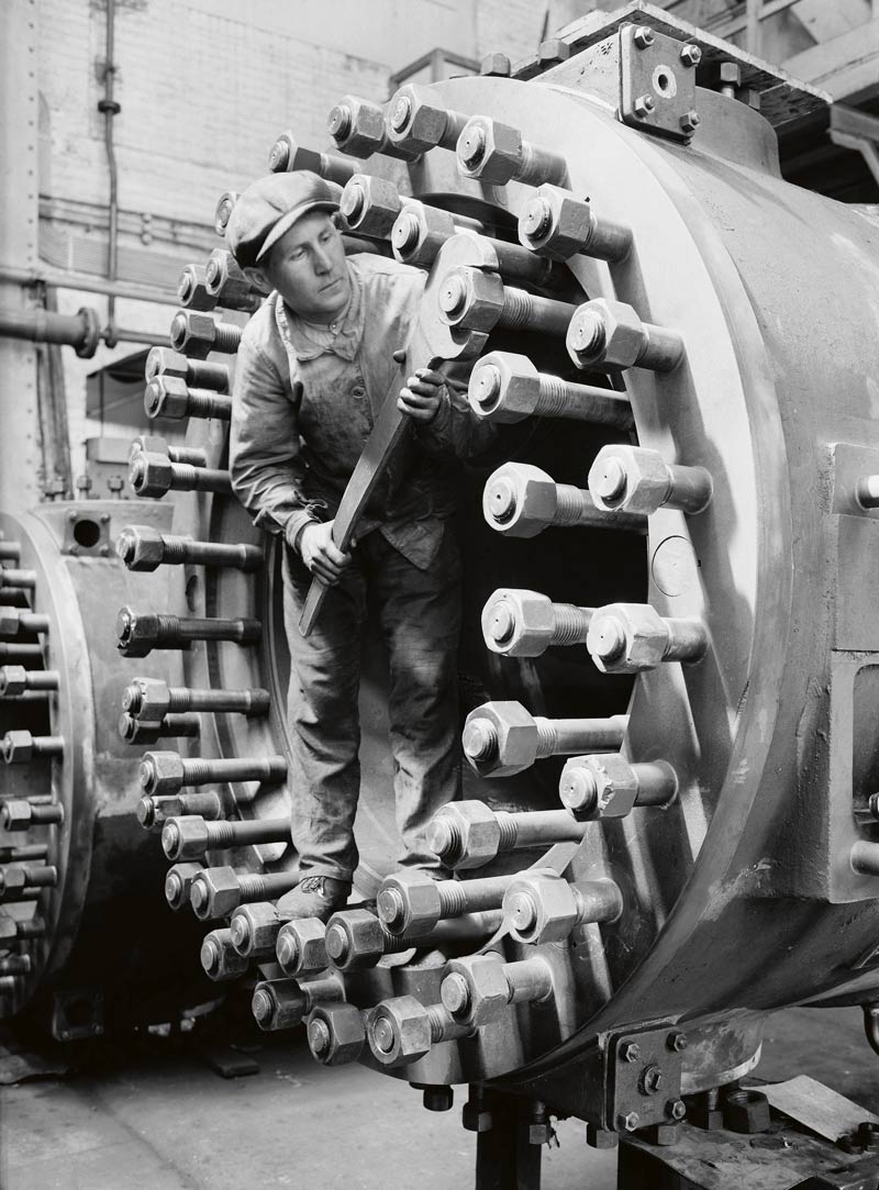 Photo ancienne : un ouvrier sert des boulons.