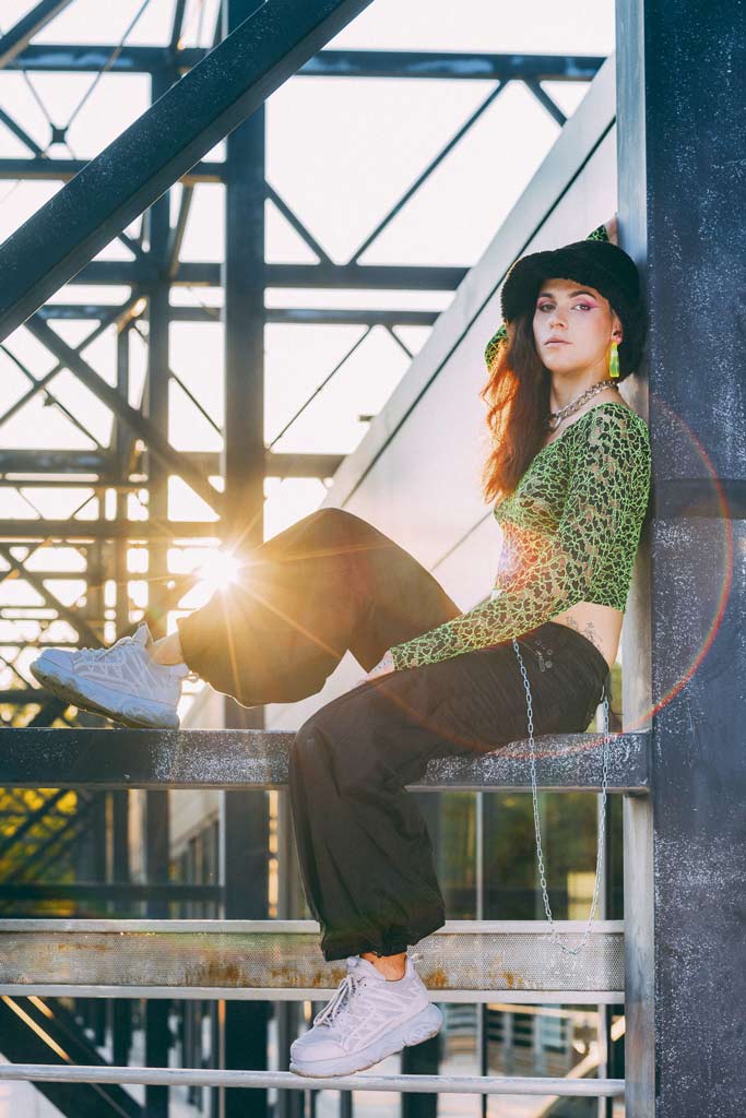 La chanteuse M4uv3 pose dans un environnement industriel alors que le soleil se couche.