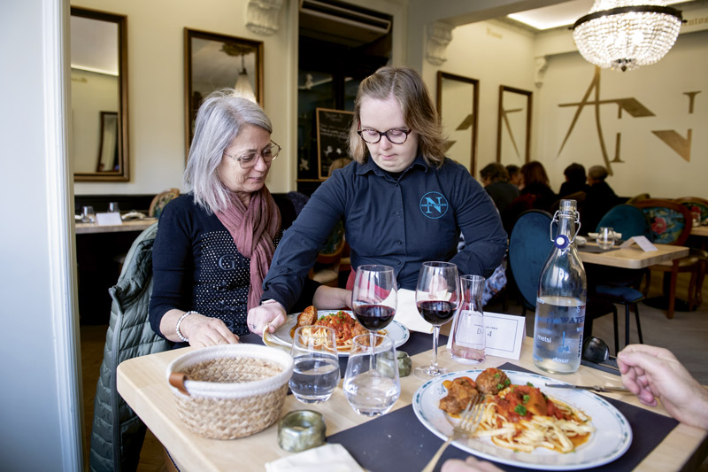Une serveuse en situation de handicap sert une dame à sa table.
