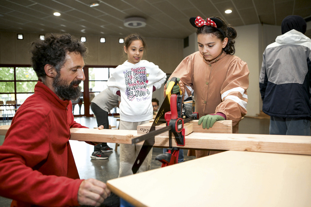 Des enfants, accompagnés d'un professionnel, découpent du bois.
