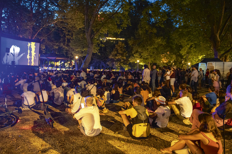 Le public regarde un grand écran dans le jardin de ville. 