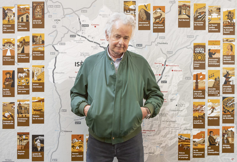 Loustal pose devant des miniatures des panneaux d'autoroute.