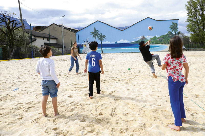 Un groupe d'enfants et d'adultes jouent au beach volley.