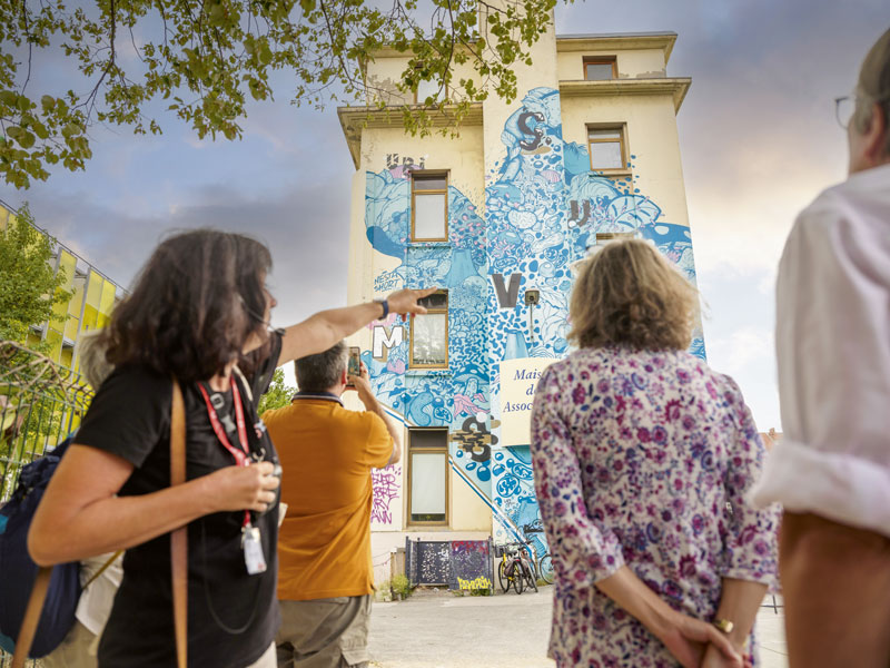 Des personnes écoutent des explications sur la façade de la Maison de la Vie Associative et Citoyenne.