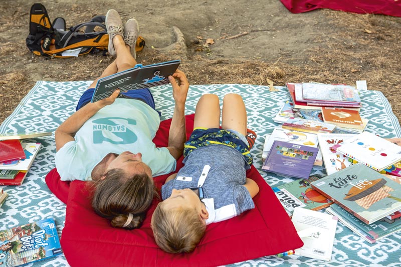 Une femme lit un livre à un enfant. Ils sont allongés dans un parc.