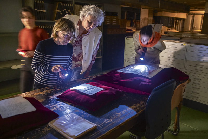 Des visiteurs lisent des documents à la lampe de poche. 