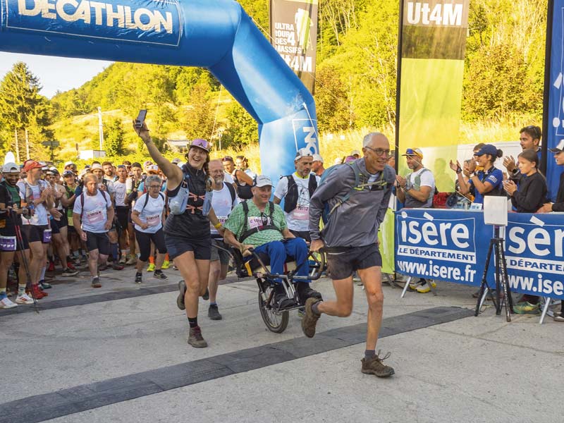 Une personne en fauteuil est tractée par des coureurs au départ de l'UT4M.