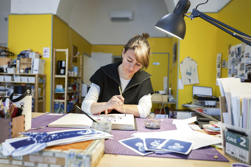 Emilie Wallaert dessine à l'encre de Chine sur un cahier d'esquisses à son bureau.