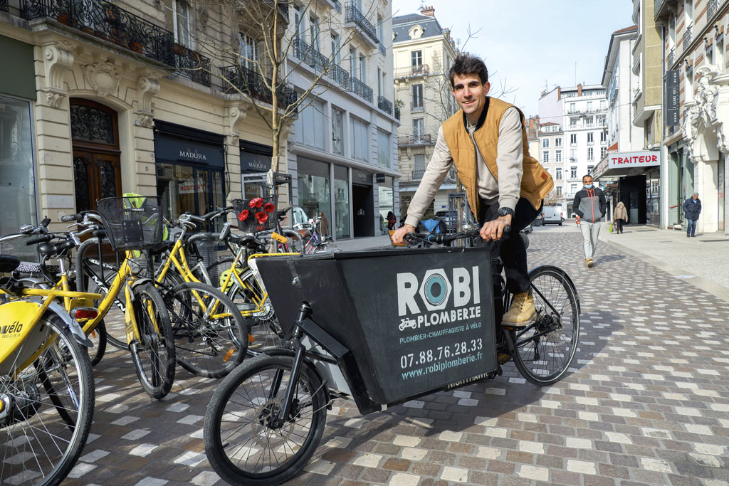 Le plombier prend la pose sur un vélo cargo. 