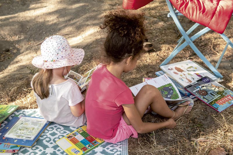Deux petites filles lisent par terre dans un parc.