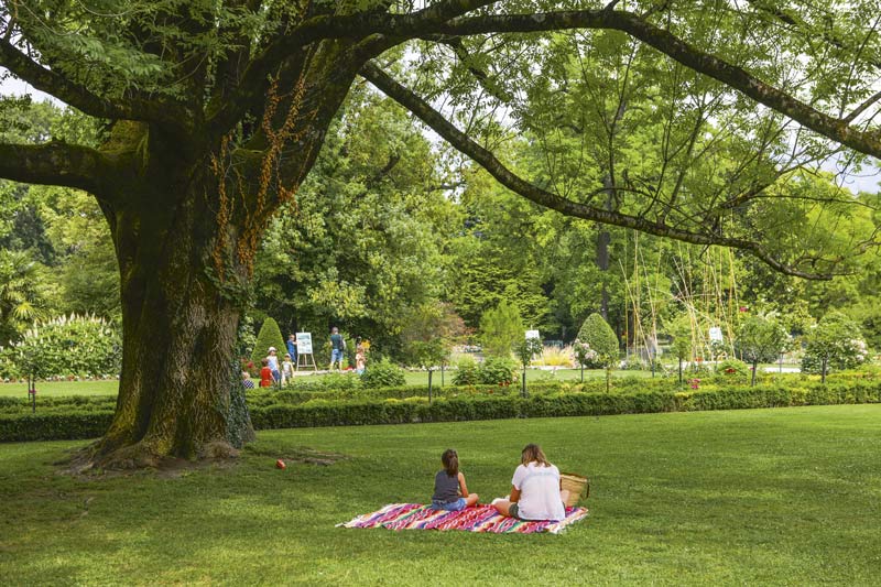 Une femme et une enfant sont assise dans l'herbe au pied d'un arbre.