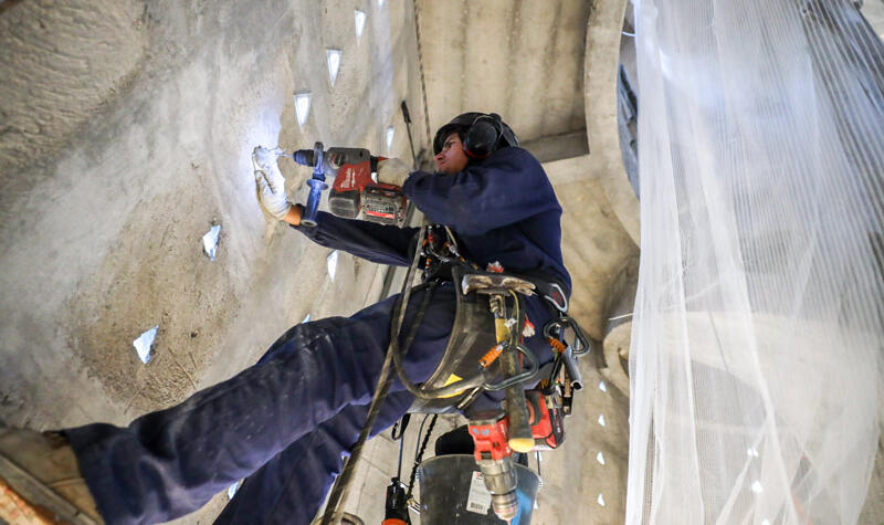 Un ouvrier suspendu dans son baudrier recouvre les claustras.
