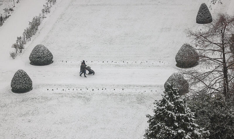 Une personne marche avec une poussette entre les allées enneigées.