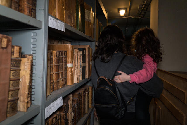 Photo d'une mère portant son enfant entre les rayonnages de livres de la bibliothèque