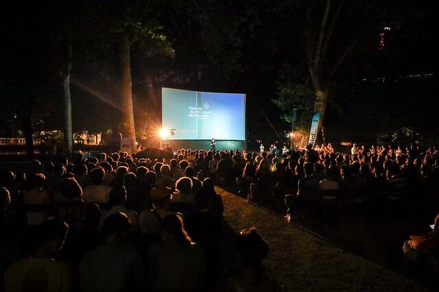 Photo d'une foule installée dans des chaises longues devant un grand écran de projection.