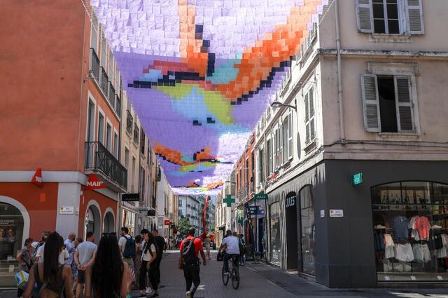 Photo du ciel de rue composé de bandes de tissus coloré, formant des motifs d'oiseaux.