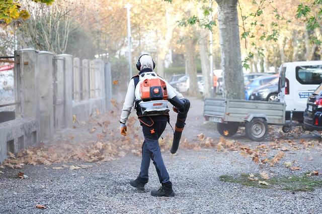 Un agent est en train de souffler des feuilles sur un trottoir.