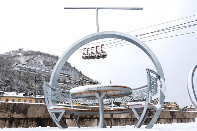 Vue sur les bulles du téléphérique et la Bastille sous la neige. En premier plan, un banc en forme de bulle.