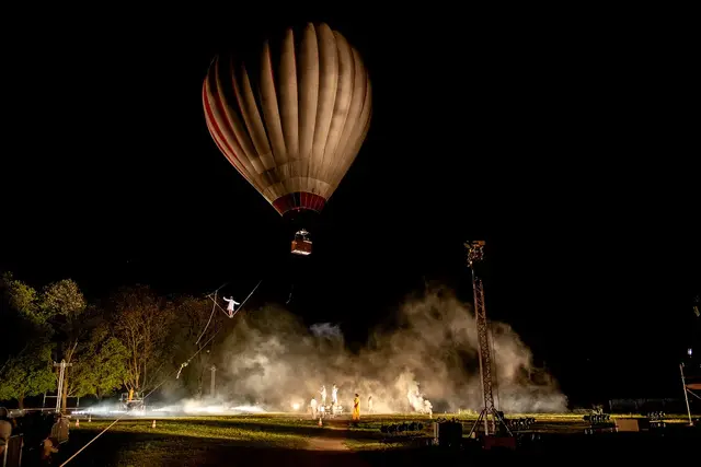 Une montgolfière survol le parc tandis qu'une funambule grimpe sur un fil reliant le sol à la montgolfière