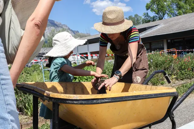 Photo d'une enfant et d'une jardinière de la ville en train de manipuler du terreau dans une brouette