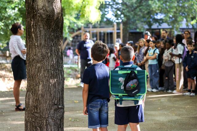 Des élèves avec leur cartables regardent un groupe de personnes.