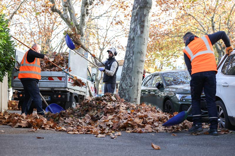 Trois agents ramassent les feuilles mortes dans une rue.