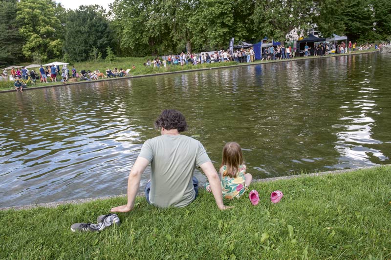 Un adulte est un enfant sont assis dans l'herbe au bord du bassin du parc Pompidou.